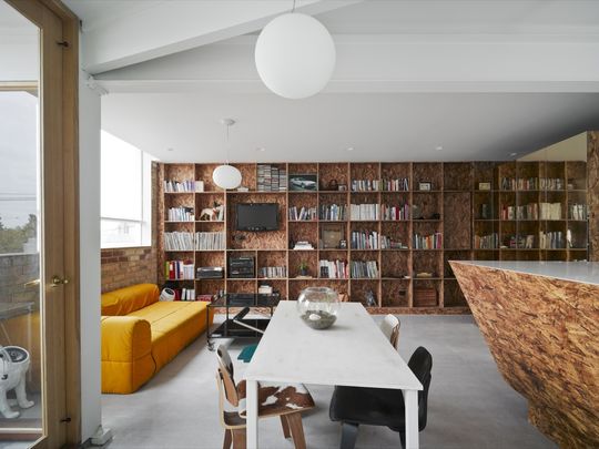 Oriented strand board bookshelves take up the entire wall of the small but not cramped living area in the project Cubby House