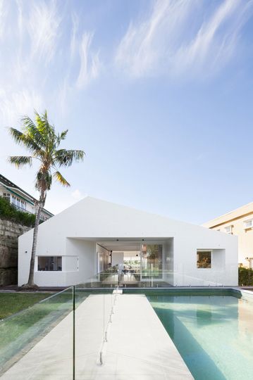 A minimalist white facade compliments a pool in the backyard of House Capple