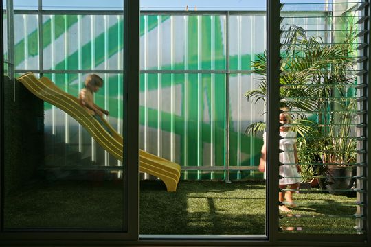 Michael and Cat's children play on a yellow slide incorporated into Polygreen's deck covered in artificial turf