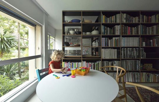 Potts Point Apartment dining area receives light from a nearby window, and is separated from the kitchen by a full height bookshelf