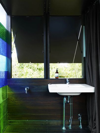 The shower room off the master bedroom is simple with dark timbers, highly saturated colored glass and openable shutters