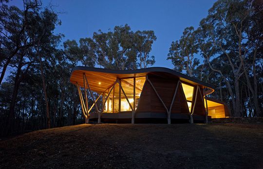 The small bush house lit up at night shows off its timber structure